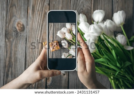 Woman take picture of bouquet of white tulips and gift box.