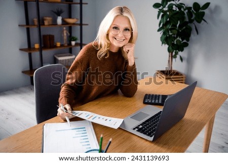 Photo of blonde hair mature age smiling business lady at workplace desktop growth marketing manager analyzing charts in home room office