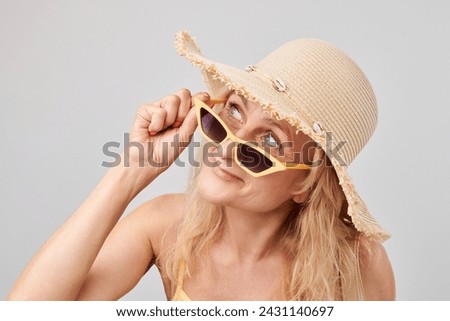 Woman with sunglasses and straw hat smiling on a light background.