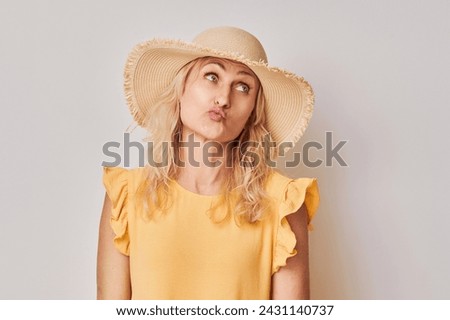 Woman in yellow blouse and straw hat with a pensive expression, isolated on a light background.