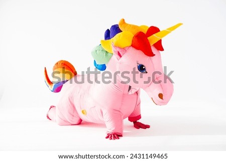 Giant pink rainbow inflatable unicorn costume on knees and with palms on floor and perfect Halloween dress for adult party events isolated against white background