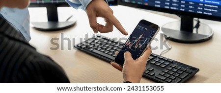 A cropped image of skilled businessman analysis growth stock graph displayed in mobile phone while discussion about financial investment at stock market with computer displayed graph. Burgeoning.