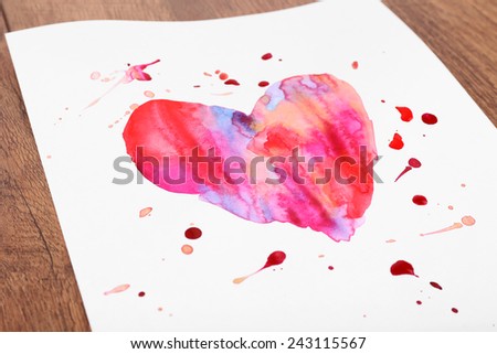 Painted heart on sheet of paper on wooden table background