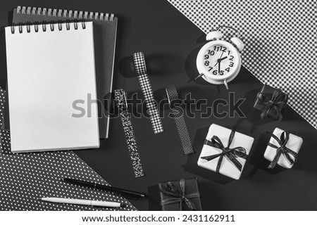 Notepads and pens and alarm clock on a black background. Deco tapes and decorative paper and gift boxes. It's time to give presents.