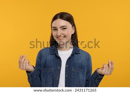 Happy woman showing money gesture on orange background