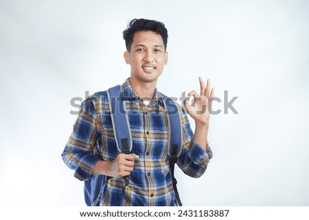 Smiling happy young Asian boy student wearing casual clothes and backpack showing ok sign, making approval gesture with finger isolated on white background. high school university college concept