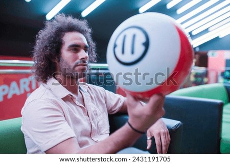 Attractive young man in casual outfit and curly hair, holding bowling ball, looking away while spending time in bowling club.