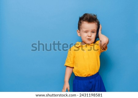 A little boy is talking on a mobile phone. Studio photo on a blue background.
