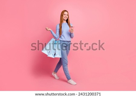 Full size photo of lovely pleasant girl walk with shopping bags to empty space hold smartphone in hand isolated on pink color background