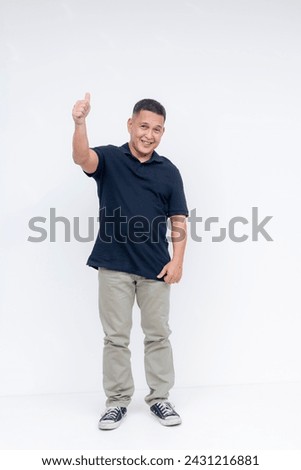 Full-body portrait of a cheerful middle-aged Asian man giving a thumbs up sign, standing against a white background.
