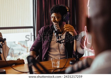 Happy radio host wearing headphones is having a vibrant conversation with a guest in a radio show studio. The mood is cheerful, epitomizing the lively dynamics of talk shows and live broadcasts.