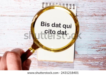Bis dat qui cito dat It is translated from Latin as The one who gives twice is the one who gives quickly through a magnifying glass on a notebook