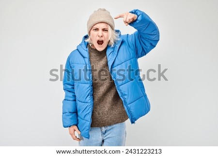 Woman in blue jacket and beanie showing strength and confidence on a plain background.