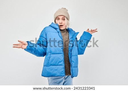 Woman in blue winter jacket and beanie shrugging with a puzzled expression on a white background.