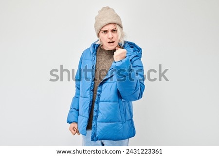 Woman in winter attire screams with anger threatens with fist against a white background.