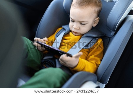 Little boy using smart phone while sitting in car back seat.