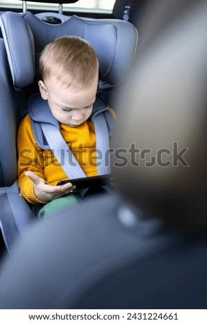 Little boy using smart phone while sitting in car back seat.