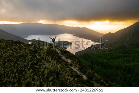 A symbol of success, an adventurous man raises his hands above his head at sunrise, showing happiness in the moment at Lagoa do Fogo on São Miguel Island, Azores. A unique moment.