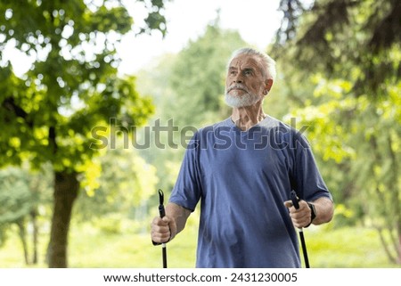 An active elderly man with trekking poles walks in a serene park, showcasing fitness and enjoyment of nature. Royalty-Free Stock Photo #2431230005
