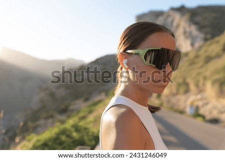 Closeup cropped photo of young caucasian female athlete in sportive outfit wearing sunglasses looking at he camera while relaxing after jogging running outdoors in the mountains forest