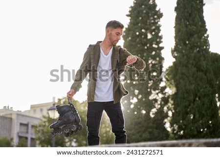 sporty man in urban clothes looking at a watch with inline skates in his hand