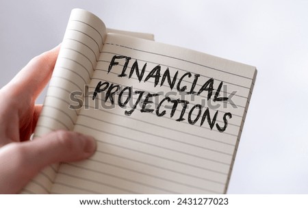 Close-up of a persons hand holding an open notebook with the words Financial Projections written on the lined paper in capital letters, symbolizing strategic planning and future growth of a business.