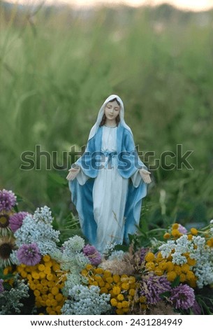 Our Lady figurine and flowers outdoor, abstract natural background. Blessed praying Mother of God, Grace Virgin Mary statue. Herbal consecration - customs on Assumption of Mary day. religion ritual