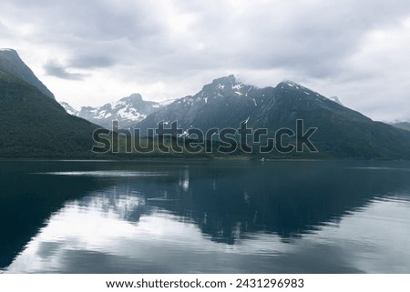 The stillness of a Norwegian fjord reflects the cloudy sky and shadowy mountains, creating a contemplative and moody landscape tableau Royalty-Free Stock Photo #2431296983
