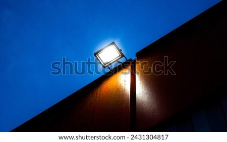 Spotlight, LED lamp, industrial glowing lantern on the wall of a building at night. Royalty-Free Stock Photo #2431304817