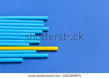 One yellow stick among blue ones on color background. Concept of uniqueness