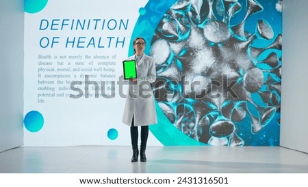 A woman in a white coat stands in front of a drug product on a large digital screen. A female scientist demonstrates a tablet with a green screen and gives a scientific lecture.
