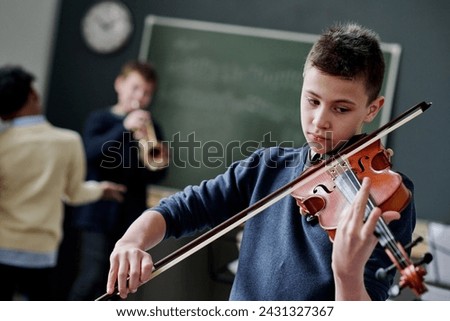 Selective focus dutch angle shot of modern teen boy playing violin during music class at school Royalty-Free Stock Photo #2431327367