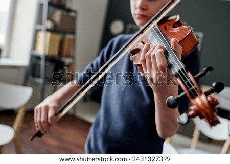 Selective focus dutch angle shot of teen boy practicing violin at music class in classroom Royalty-Free Stock Photo #2431327399