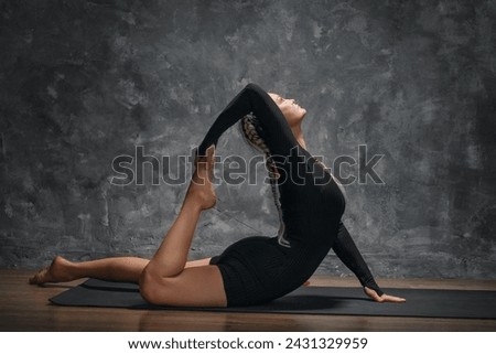 Athletic attractive woman training in the room lying on a mat, performing an exercise for body flexibility, doing a backbend