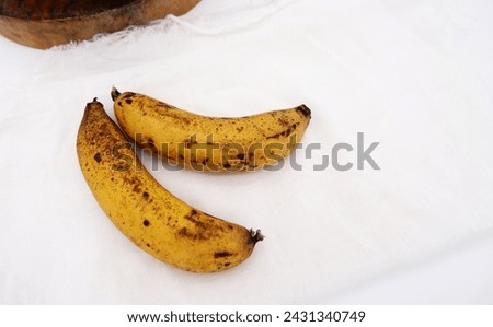 Ripe bananas placed on cheesecloth with rustic style kitchen. This type of ripe banana is ready for baking cupcakes. Two pieces of banana with white fabric or cheesecloth. Fruit image with copy space. Royalty-Free Stock Photo #2431340749