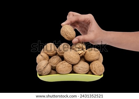 Hand Selecting a Walnut from a Vibrant Bowl Full, This image captures a moment where a hand delicately selects a walnut from a vibrant bowl full of them. The walnut natural, textured shell and golden