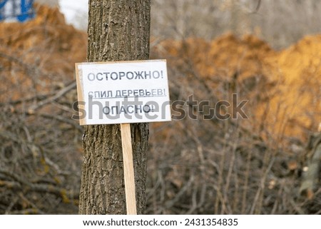 the inscription on the sign is in Russian. translation: be careful, cutting down trees is dangerous. against the backdrop of a construction site. cutting down trees during construction.