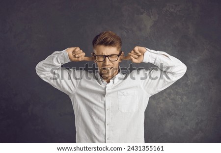 Studio shot of college or university student in glasses closing eyes and plugging ears with fingers to ignore noise, dumb stupid comments, unwanted opinions and useless unsolicited uninvited criticism