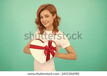 cheerful woman hold heart gift box on blue background