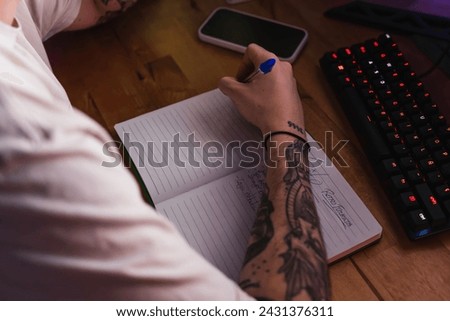 Detail shot of a tattooed graphic designer writing ideas in a notebook during his free time at home