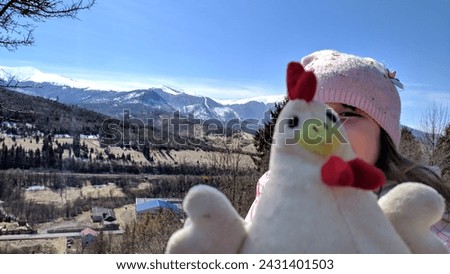A 5-year-old girl with a toy against a background of snow-capped mountains, close-up. Photo.