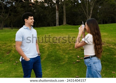 The bride is taking a picture of the groom smiling with an instant camera in the park in the middle of nature