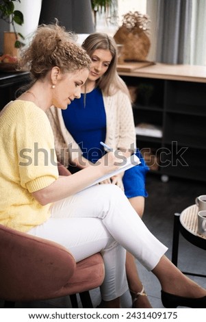 Two women engaged in coaching or psychotherapy session, one taking notes, evoking a focused learning atmosphere, and business growth. High quality photo