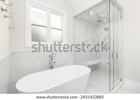 A bathroom's freestanding bathtub with a chrome faucet, marble tile on the walls and floor, and a walk-in shower with marble walls and bench. No brands or labels. Royalty-Free Stock Photo #2431423885