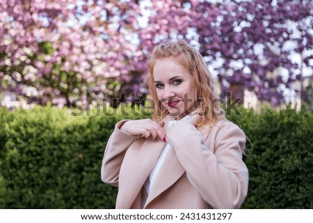 Portrait of beautiful young woman of European appearance. Strong modern woman in coat in park. Successful business woman