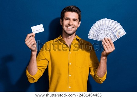 Photo portrait of handsome young guy hold money fan credit card dressed stylish yellow outfit isolated on dark blue color background