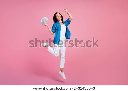 Full length photo of ecstatic overjoyed woman wear stylish shirt white pants jumping hold money win bet isolated on pink color background