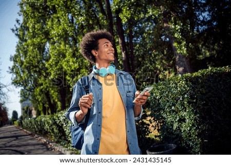 Photo of good mood dreamy guy wear denim jacket earphones communicating modern device outside urban city street