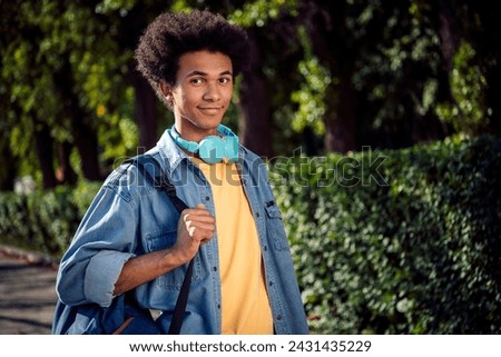 Photo of funky cheerful guy wear denim jacket earphones walking college lessons outside urban city street