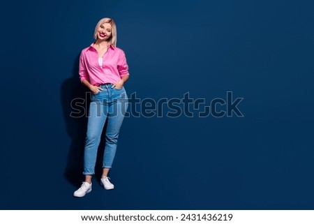 Full length photo of good mood lovely girl wear stylish shirt denim pants holding arms in pockets isolated on dark blue background